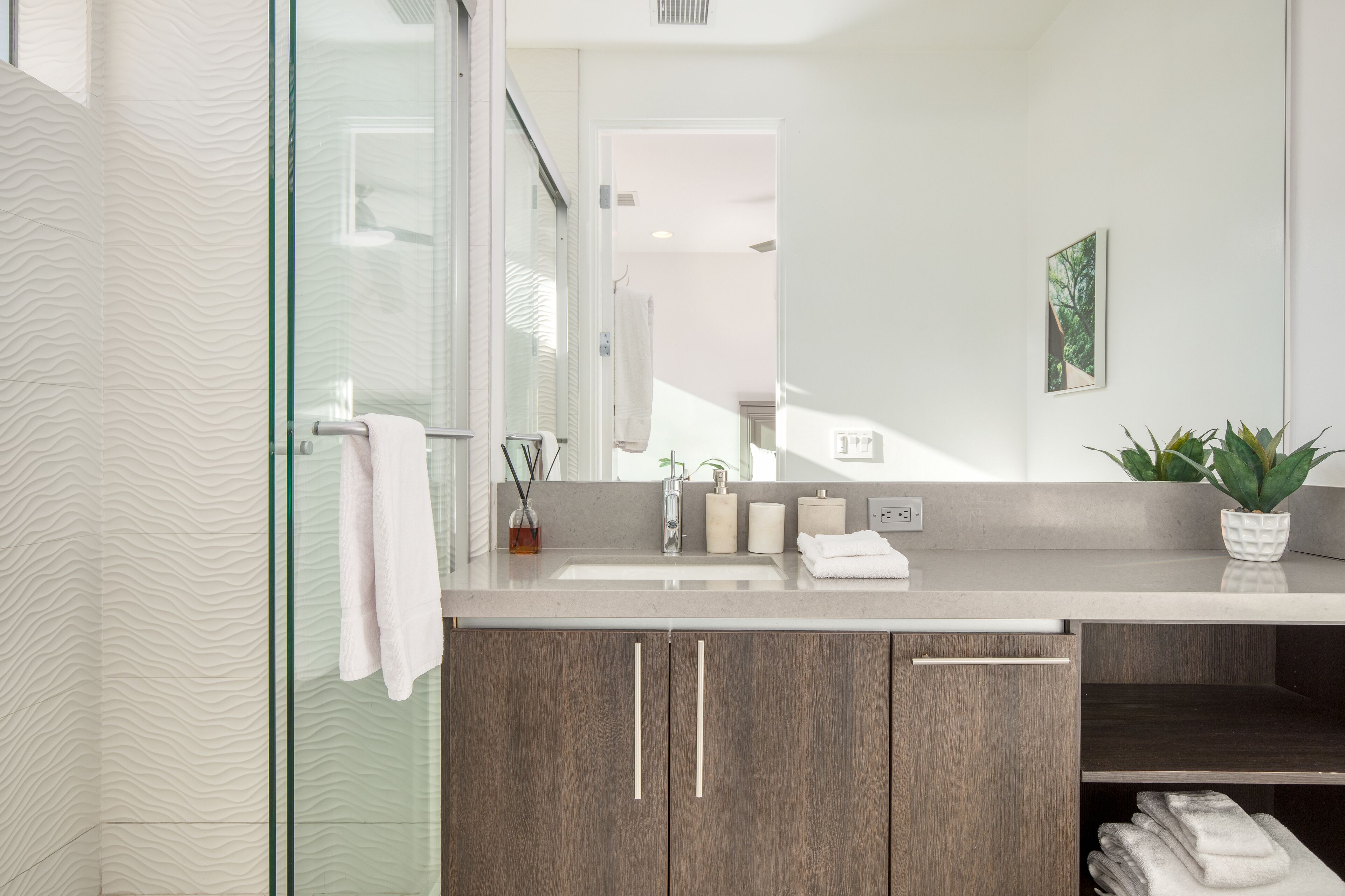 A modern bathroom with a glass shower enclosure, a large mirror, and a wooden vanity with a sink.