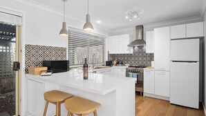 Una cocina moderna con armarios blancos, una isla central con taburetes, un horno empotrado y un salpicadero con diseño.
