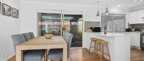 A modern kitchen with a central island, wooden dining table, and bar stools.