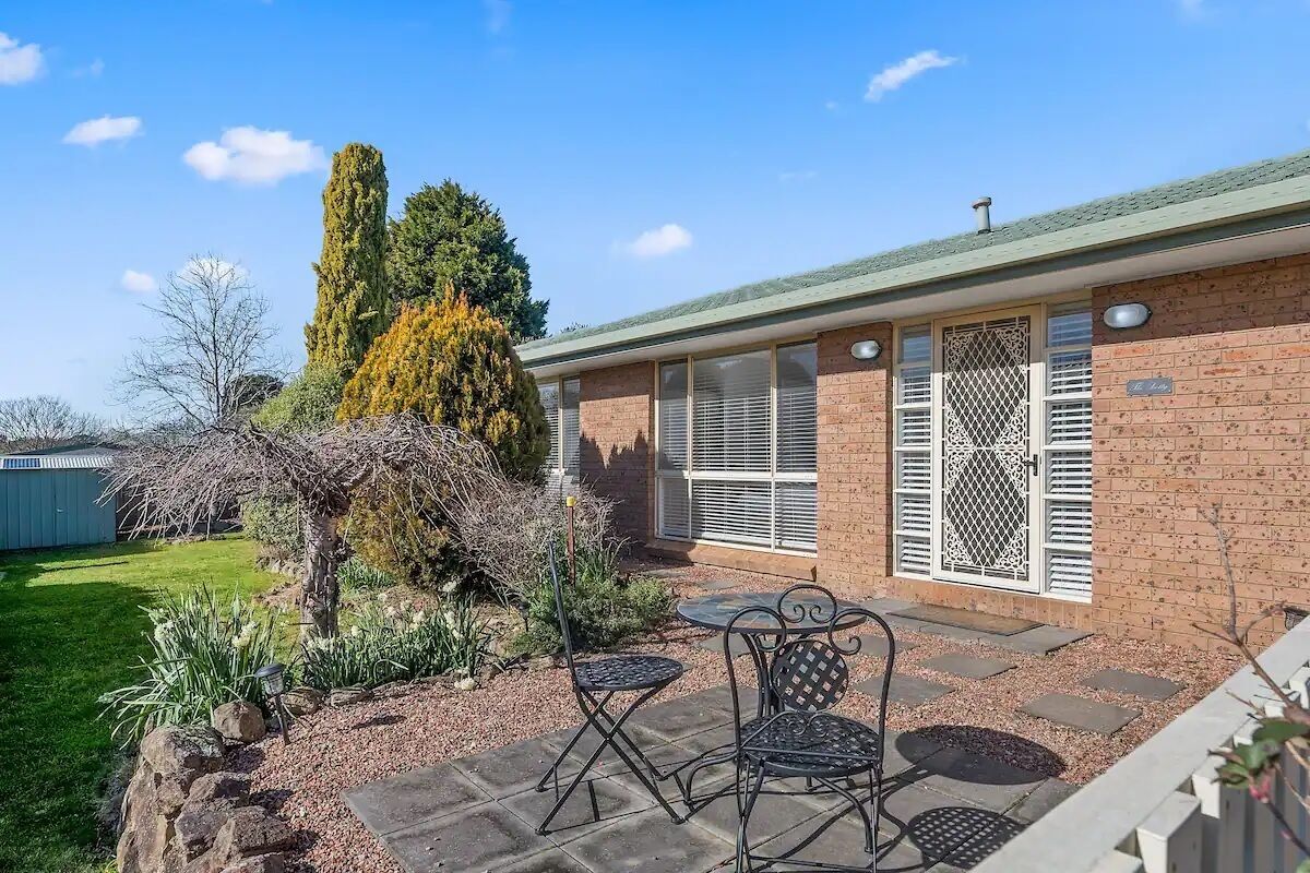 A brick house with a patio, two metal chairs, and a small garden.