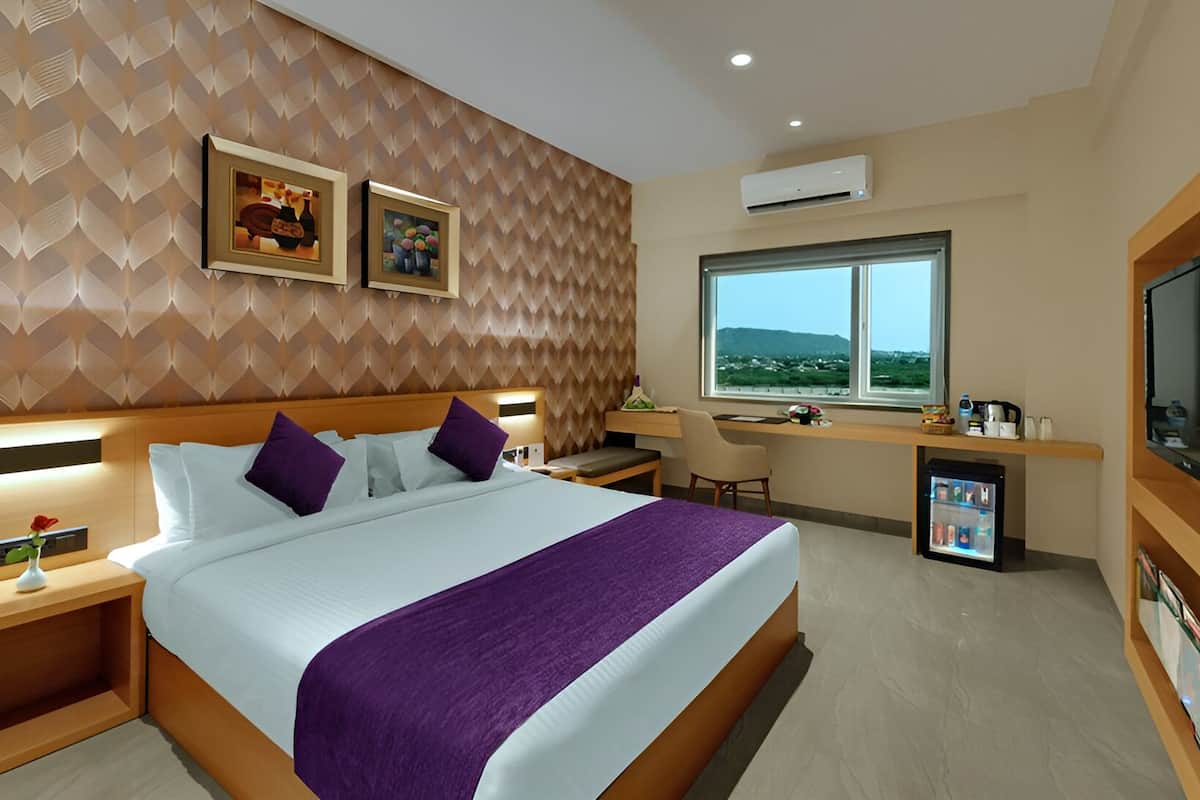 Una habitación de hotel moderna con una cama grande, un escritorio, una silla, un televisor y un ventanal con vistas.