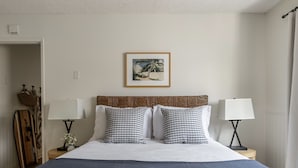 A neatly arranged bedroom with a bed, two bedside tables with lamps, a framed picture on the wall, and a suitcase on the floor. - Patio + Sunset Views + Beach Days | Right on the Water | Bay View 2 (San Diego)