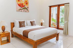 A neatly made bed with white and brown bedding, two bedside tables with lamps, a painting of flowers on the wall, and a view of greenery through a window with curtains. - Canggu Kayuma House (Canggu)