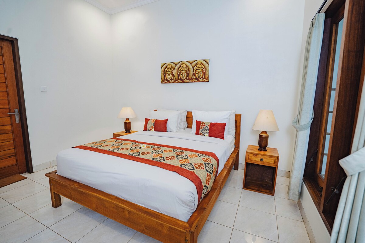A neatly made bed with a patterned bedspread, two bedside tables with lamps, and a wall-mounted artwork above the bed.