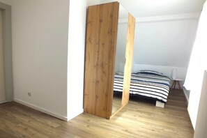 A bedroom with a wooden wardrobe, a bed with striped bedding, and a white wall. - Holiday Home in Lichtenau with Garden Bliss (Lichtenau / OT Auerswalde)
