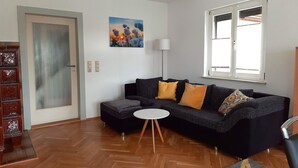 A modern living room with a black sofa, a small white table, and a wooden cabinet. - Holiday Home in Lichtenau with Garden Bliss (Lichtenau / OT Auerswalde)