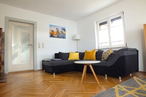 A living room with a dark grey sectional sofa, a round white coffee table, and a wooden floor. - Holiday Home in Lichtenau with Garden Bliss (Lichtenau / OT Auerswalde)