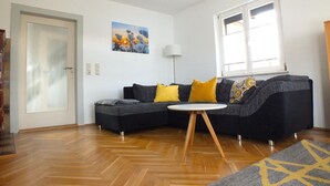 Un salón con un sofá seccional gris oscuro, una mesa de centro redonda blanca y suelo de madera.