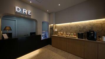 A hotel reception area with a modern design, featuring a reception desk, a coffee machine, and a counter with jars of condiments.