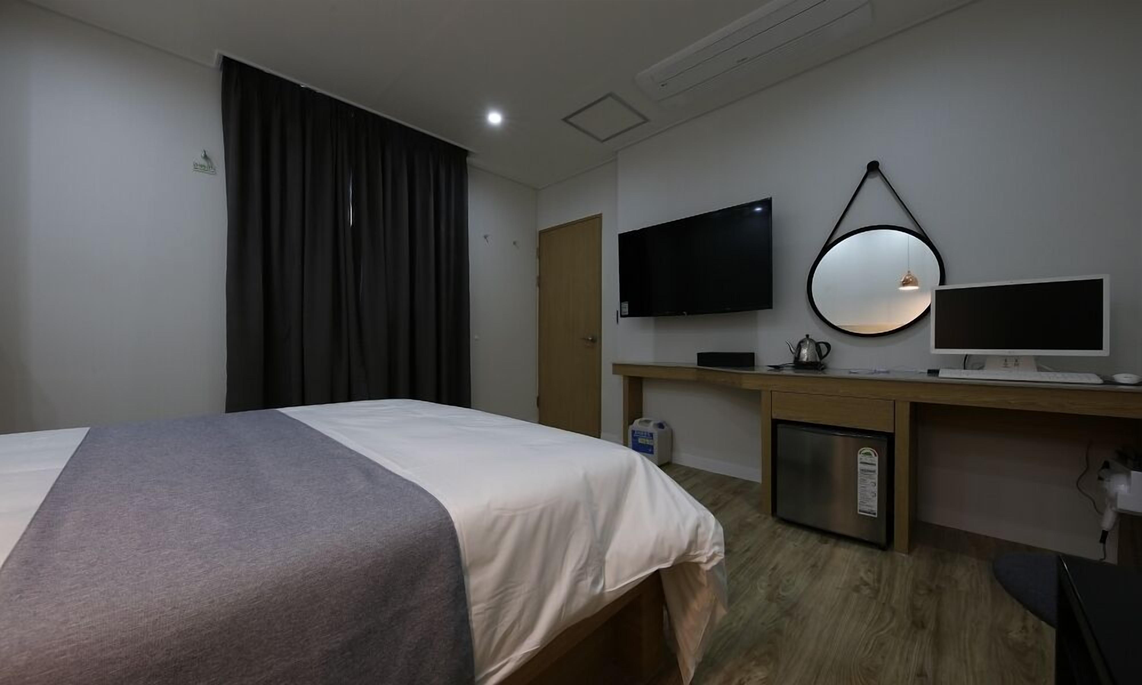 Ein Hotelzimmer mit einem Bett, einem Schreibtisch mit Computer, einem Fernseher und einem Kühlschrank.