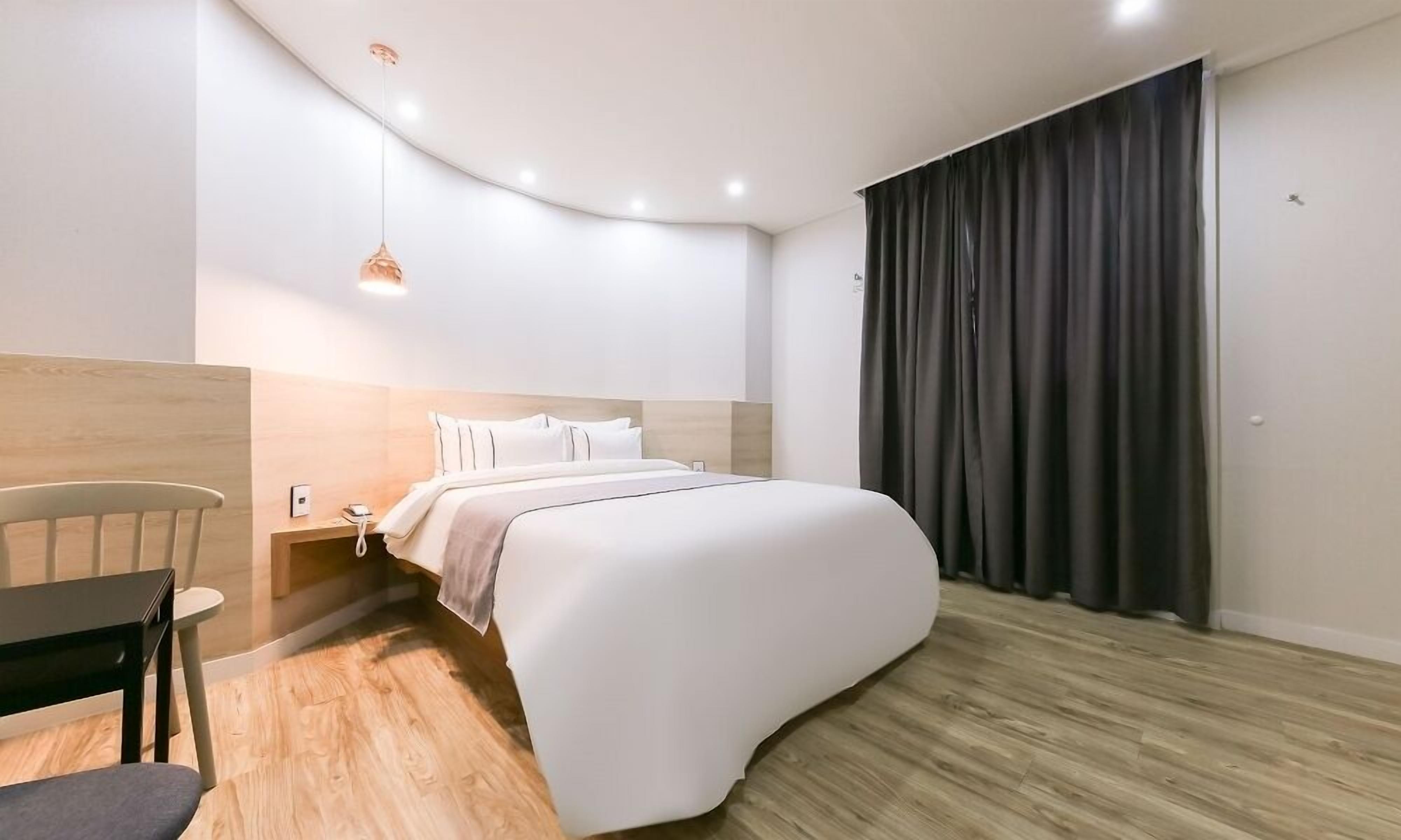 A modern bedroom with a curved bed, a wooden nightstand, a desk, and a chair.