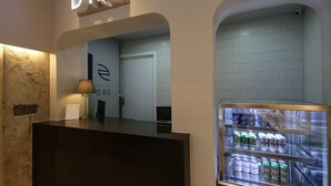 Un espace d’accueil d’hôtel au design moderne, comprenant un comptoir d’accueil, un panneau mural et un réfrigérateur pour boissons.