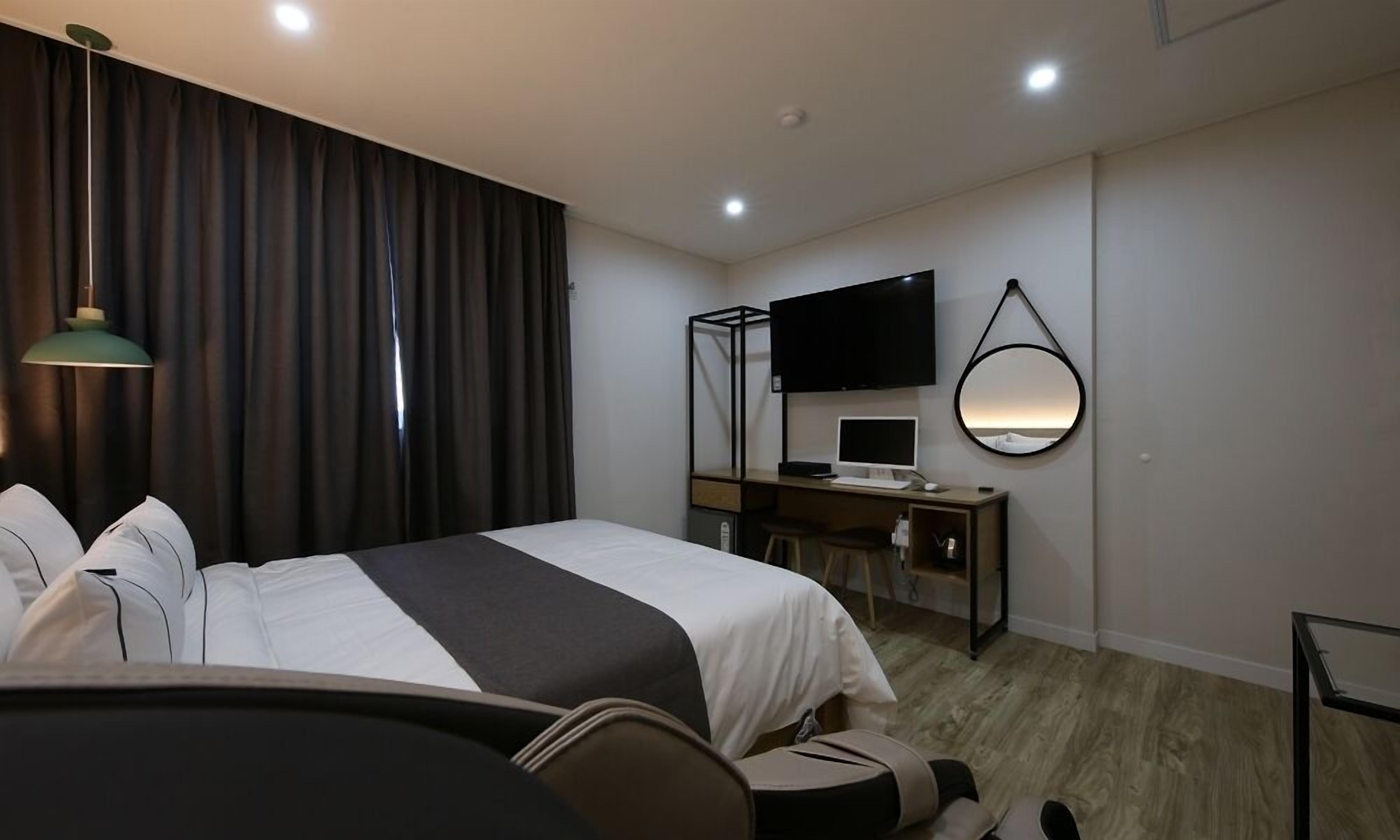A hotel room with a bed, a desk, a TV, and a mirror.
