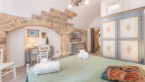 A room with a stone archway, a bed with a green bedspread, a desk with a lamp, and a wardrobe with floral designs. - Appartamento Misya - Felline (Felline)