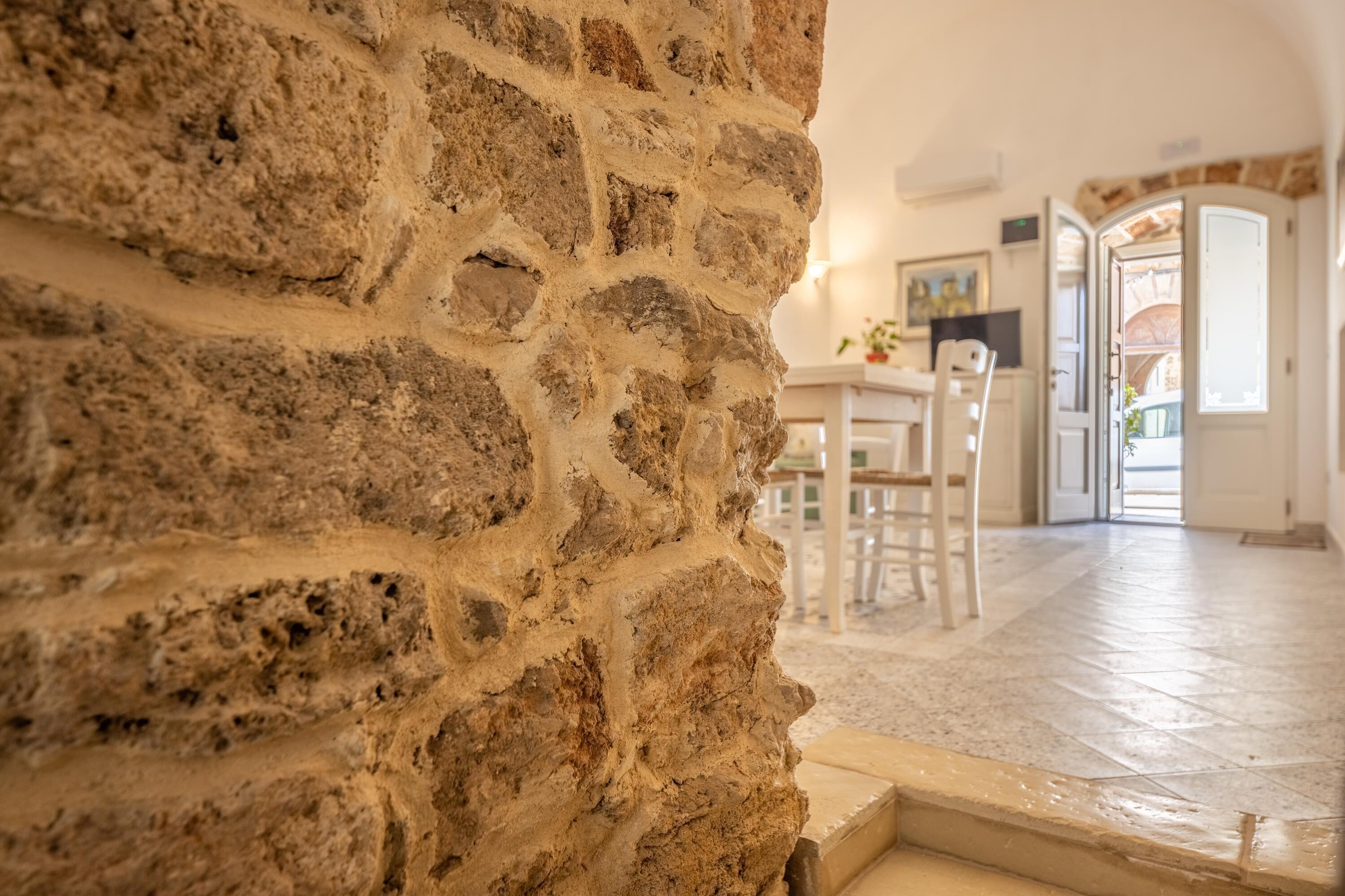 Pared de piedra en una habitación con suelo de baldosas y una puerta que da a otra zona.