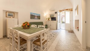 A dining area with a table set for four, a green sofa, and a television in the background. - Appartamento Misya - Felline (Felline)