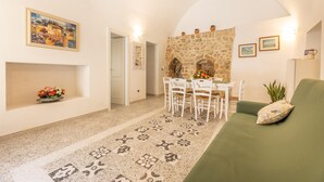 A living room with a stone fireplace, a dining area with white chairs, a green sofa, and a patterned rug. - Appartamento Misya - Felline (Felline)