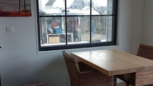 A room with a large window, a wooden table, wicker chairs, a hanging light fixture, and construction materials on the floor.