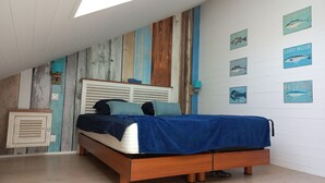 A bedroom with a sloped ceiling, a wooden bed frame, a white headboard, and a blue bedspread.