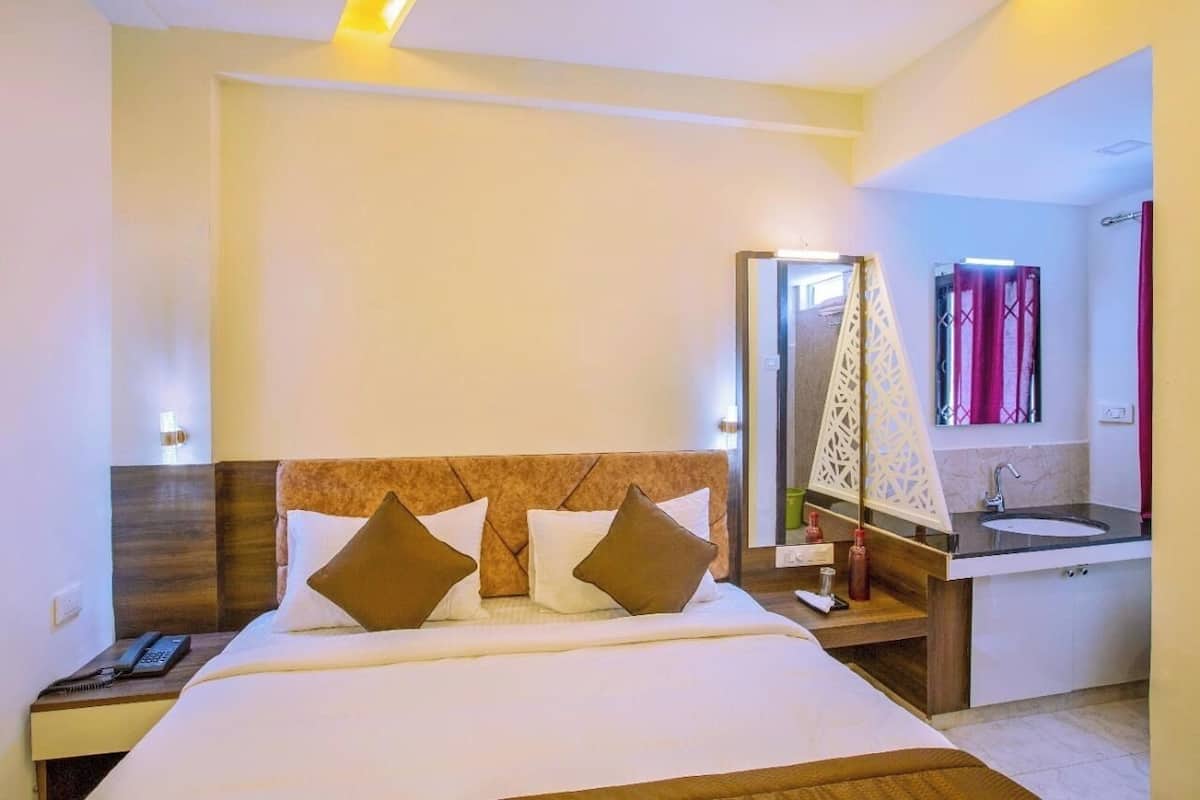 A hotel room with a bed, bedside table, and a bathroom with a sink and mirror.