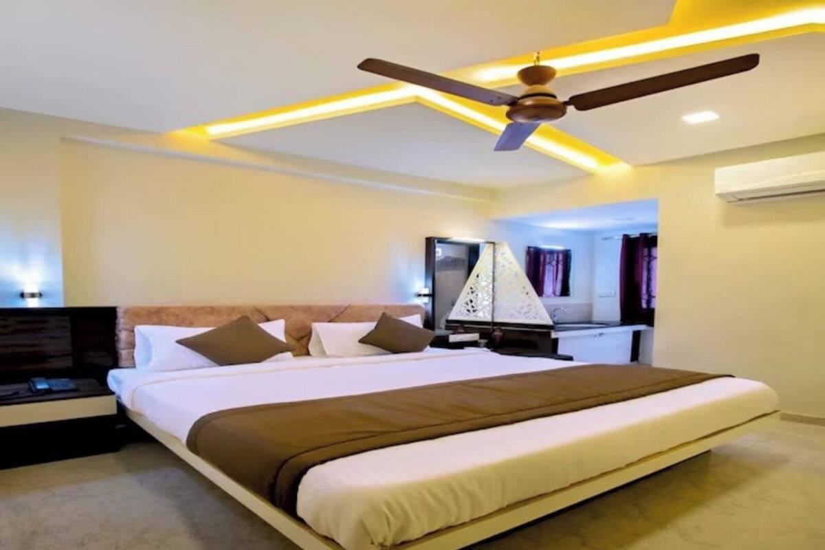 A modern hotel room with a large bed, a ceiling fan, and a TV.