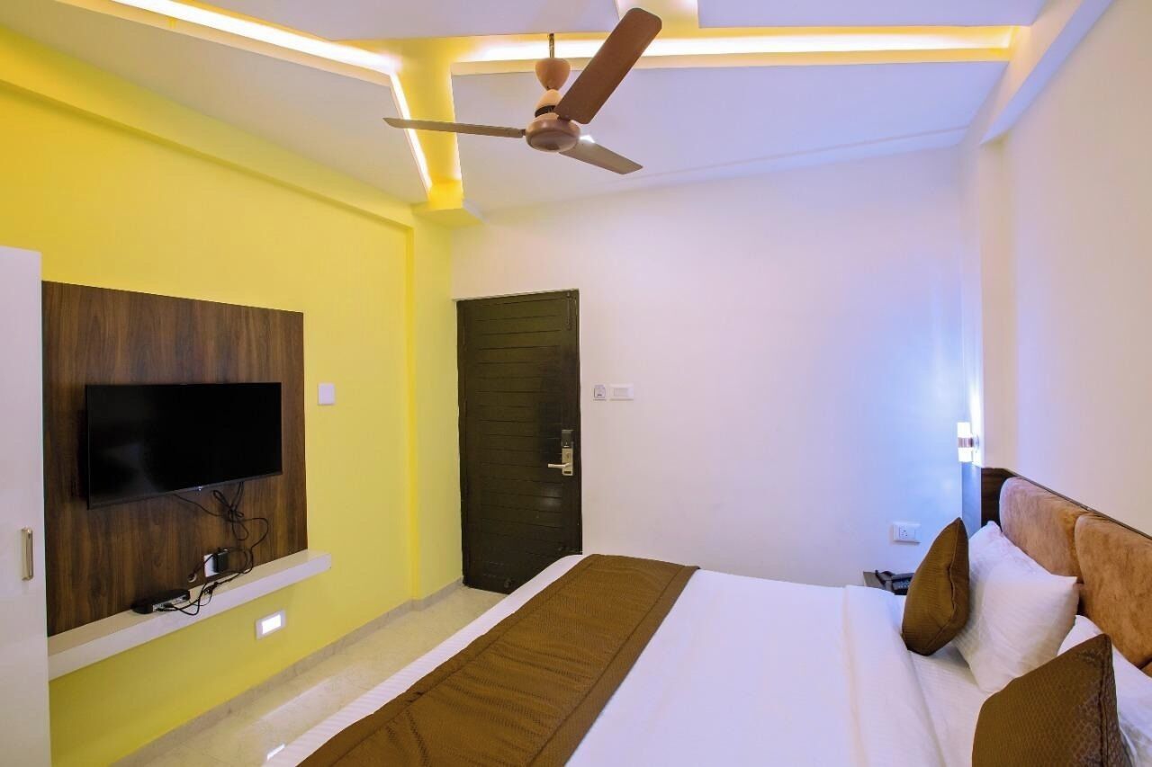 Een hotelkamer met een bed, een flatscreen televisie aan de muur, een plafondventilator en een deur.