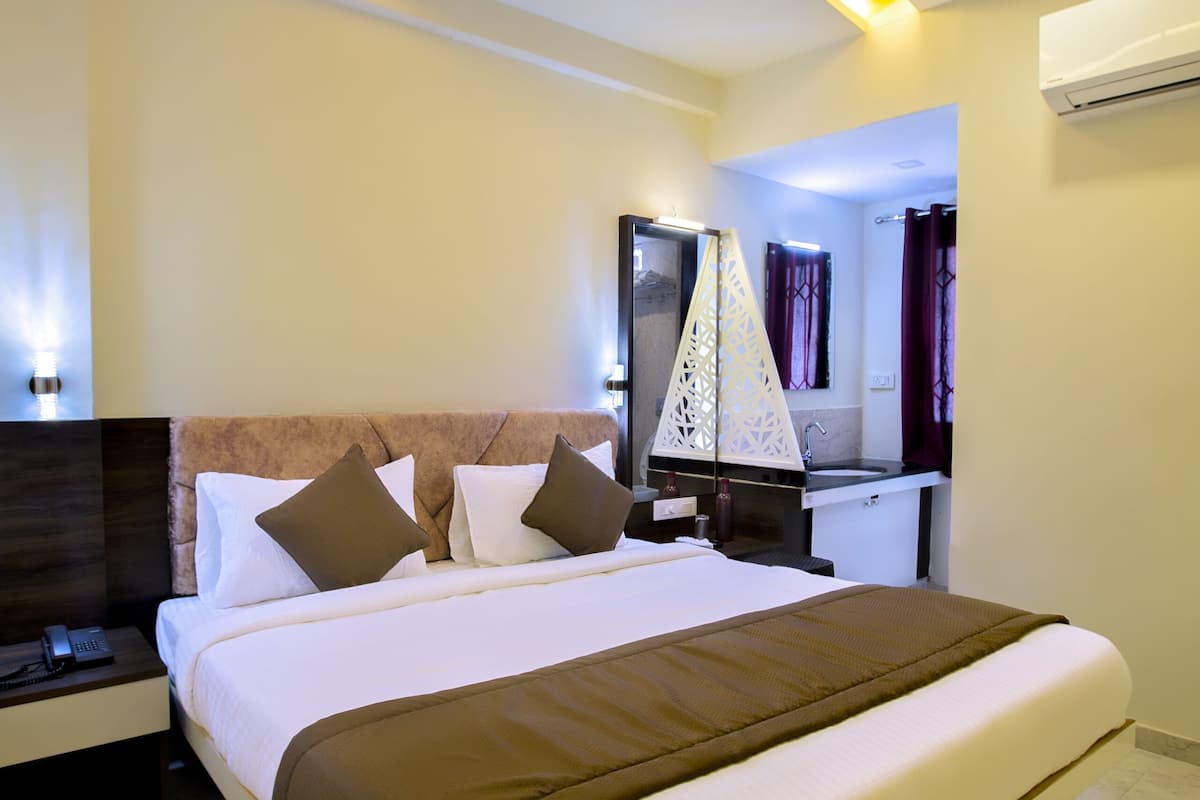 A hotel room with a bed, a ceiling fan, a nightstand, a bedside table, and a bathroom visible in the background.