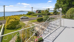 Ein Balkon mit Metallgeländer, der auf eine Straße, ein Gewässer und ein entferntes Gebirge blickt.