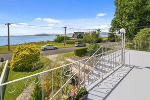 A balcony with a metal railing overlooking a road, a body of water, and a distant mountain.