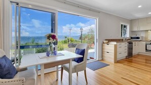 Eine moderne Küche mit einem großen Fenster, einem Essbereich mit Tisch und Stühlen und Blick aufs Meer.