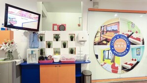 Zona de recepción de hotel con una pantalla digital mostrando un mensaje de bienvenida, un mostrador con diversos servicios y un gran cartel circular que anuncia el hotel.