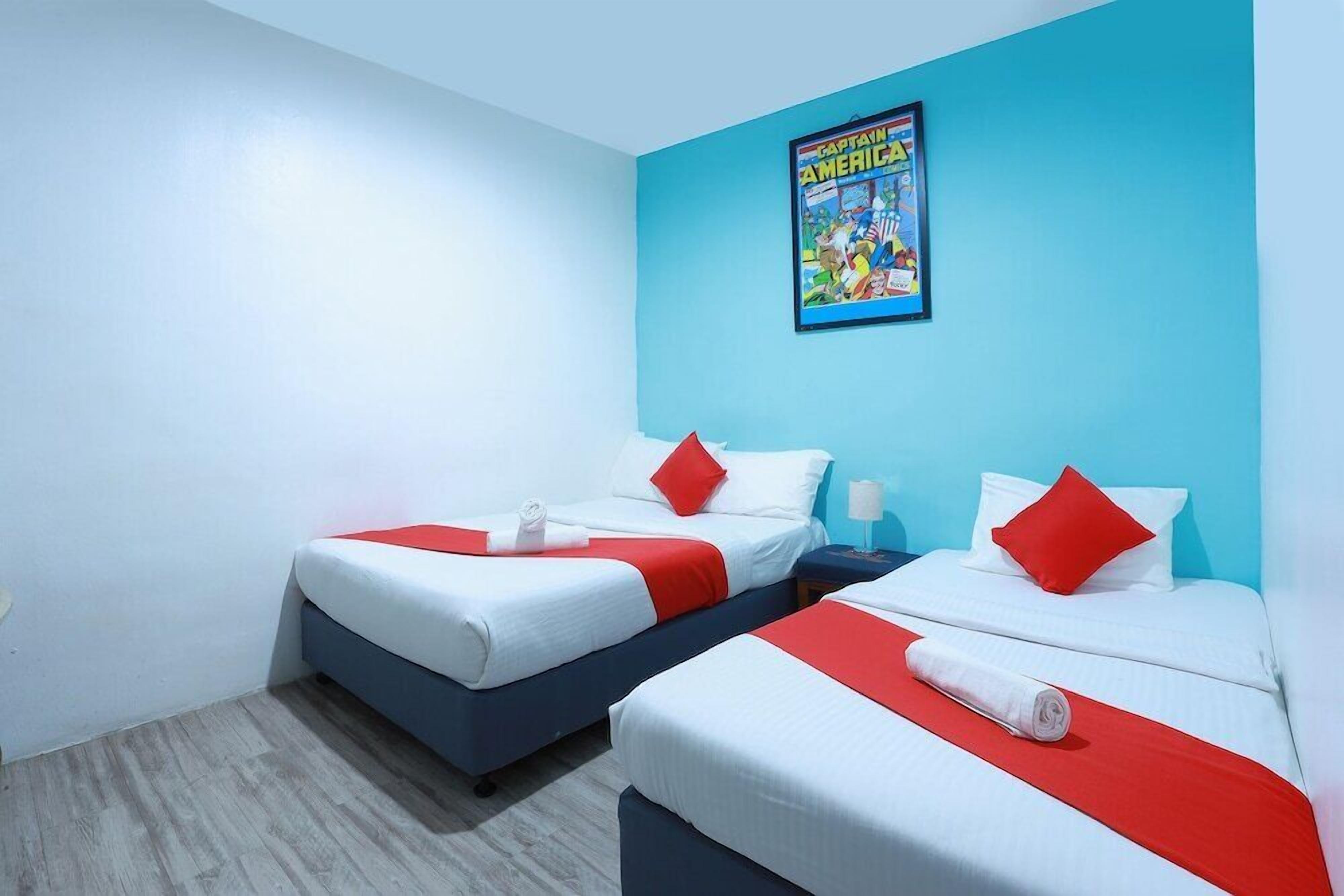 Une chambre d’hôtel avec deux lits, chacun agrémenté de draps blancs et de touches de couleur rouge, une affiche au mur et un plancher en bois.