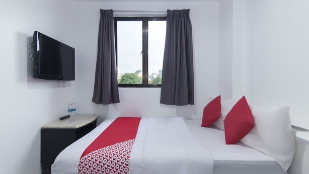 Habitación de hotel con cama, televisor montado en la pared, ventana con cortinas y una mesita con control remoto.