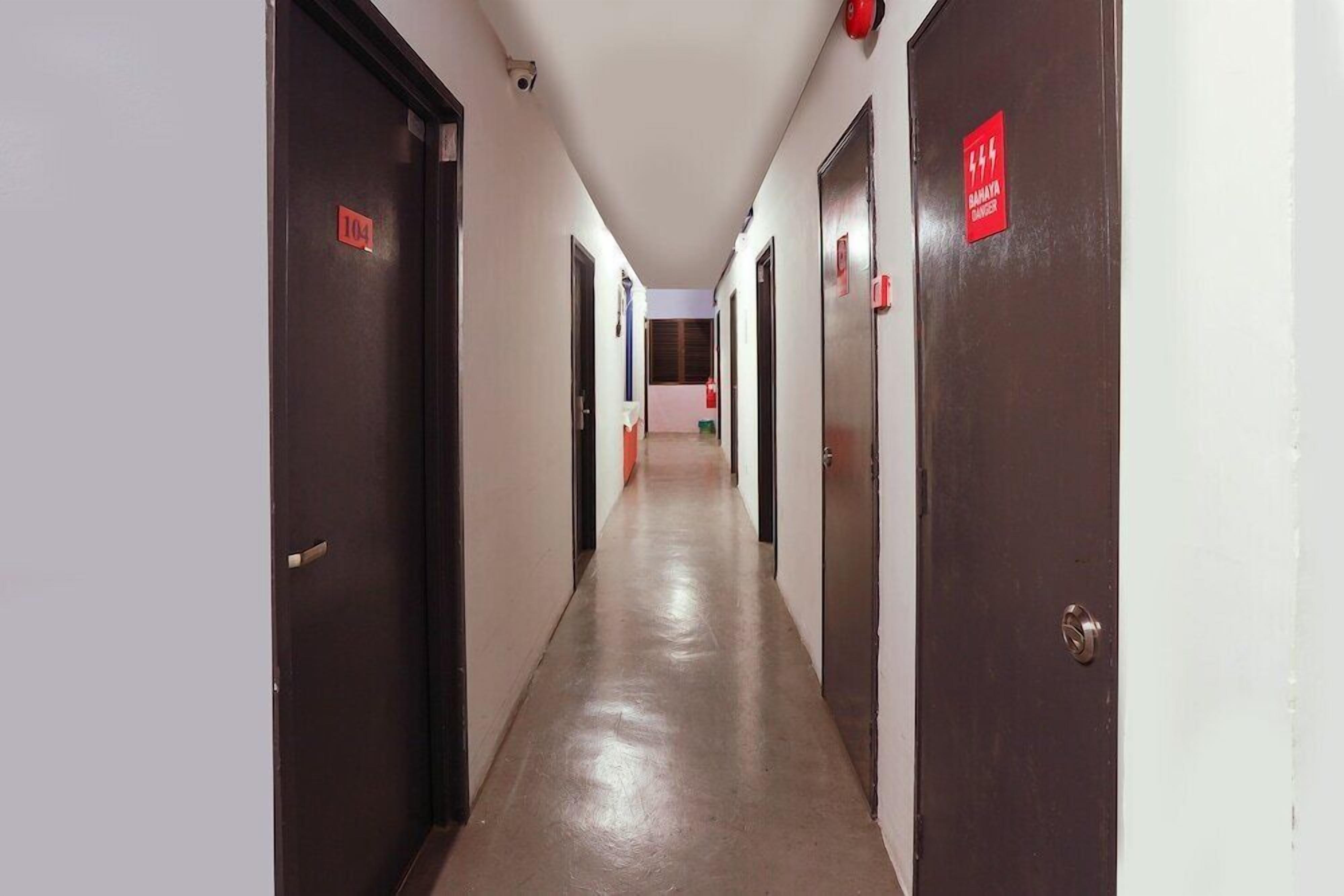 Un pasillo con puertas a ambos lados, algunas numeradas y un cartel de alarma contra incendios.