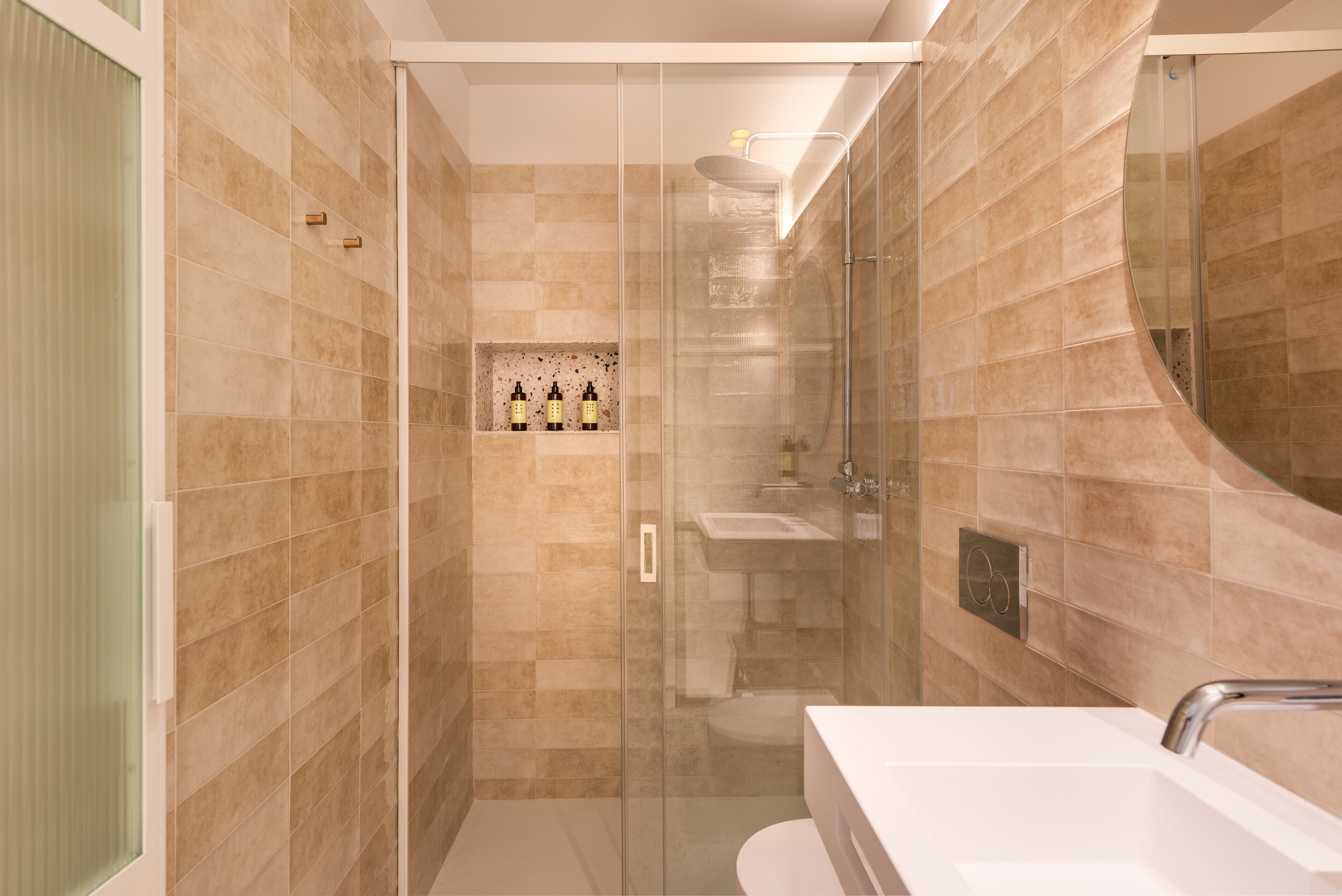 A modern bathroom with a glass-enclosed shower, a white sink, and a tiled wall.
