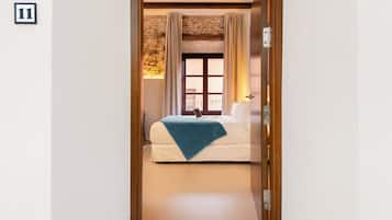 Quarto de hotel com cama, janela com cortinas, teto de madeira e o número 11 na parede.