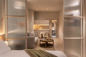 A modern hotel room with a bed, a seating area with a table, and a kitchenette in the background. - Coeo Fresca Roof Garden Signature Apartments (Málaga)