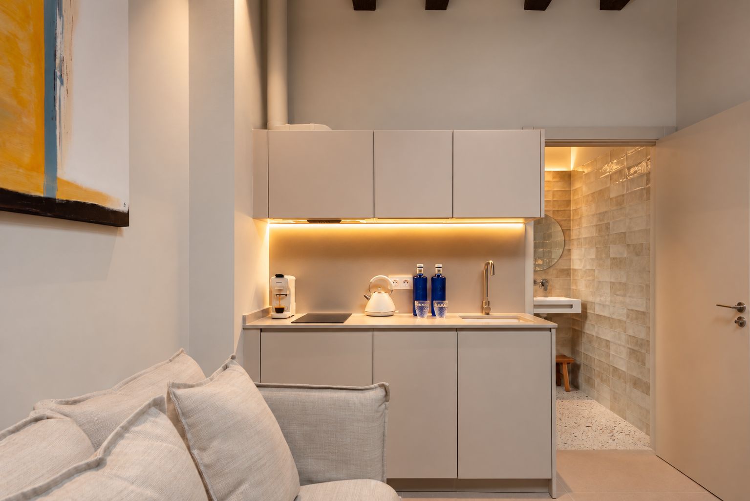 A compact kitchen with a coffee maker, two bottles, and a kettle on the counter.