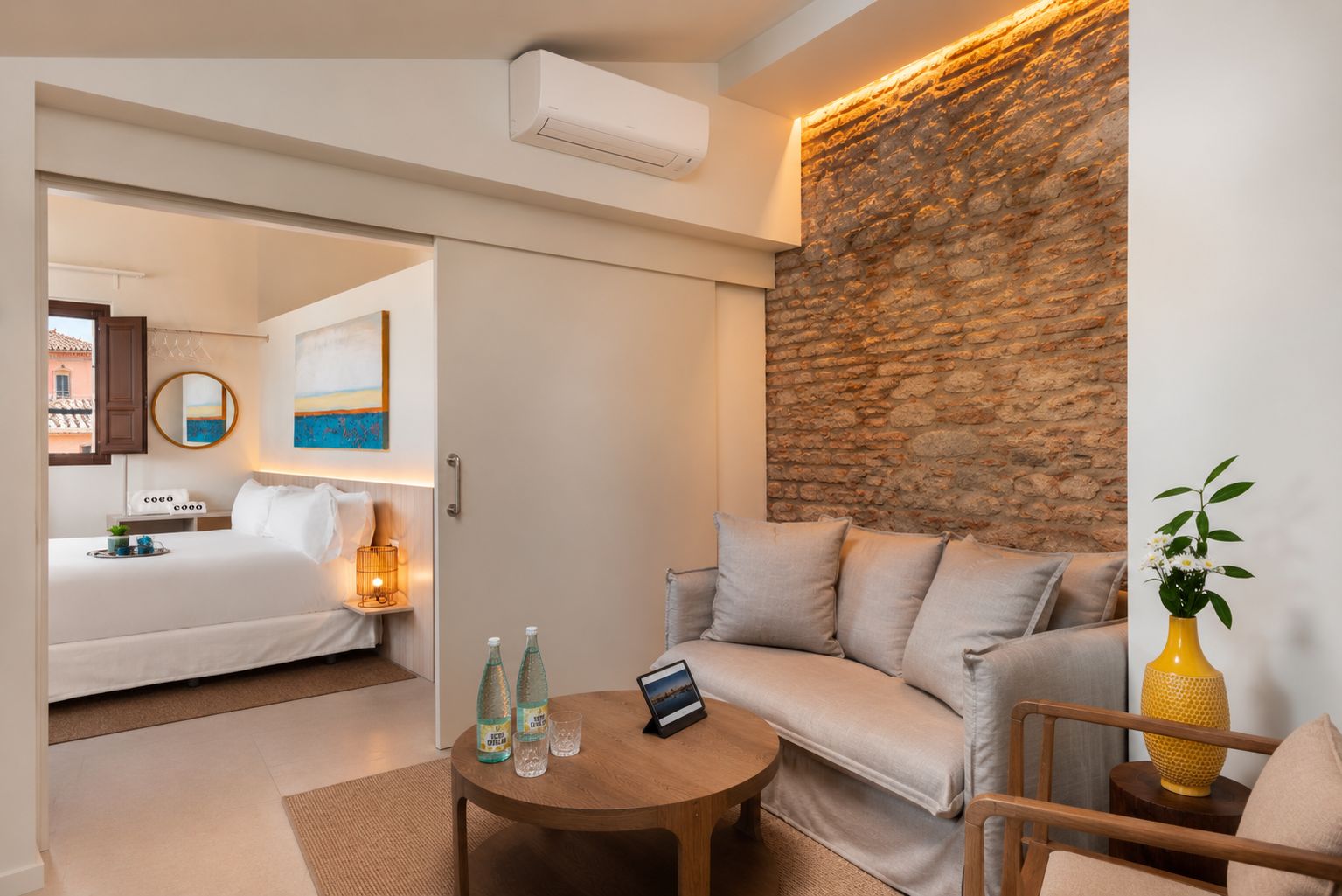 A hotel room with a bed, a sofa, a small table with a lamp, and a decorative vase.