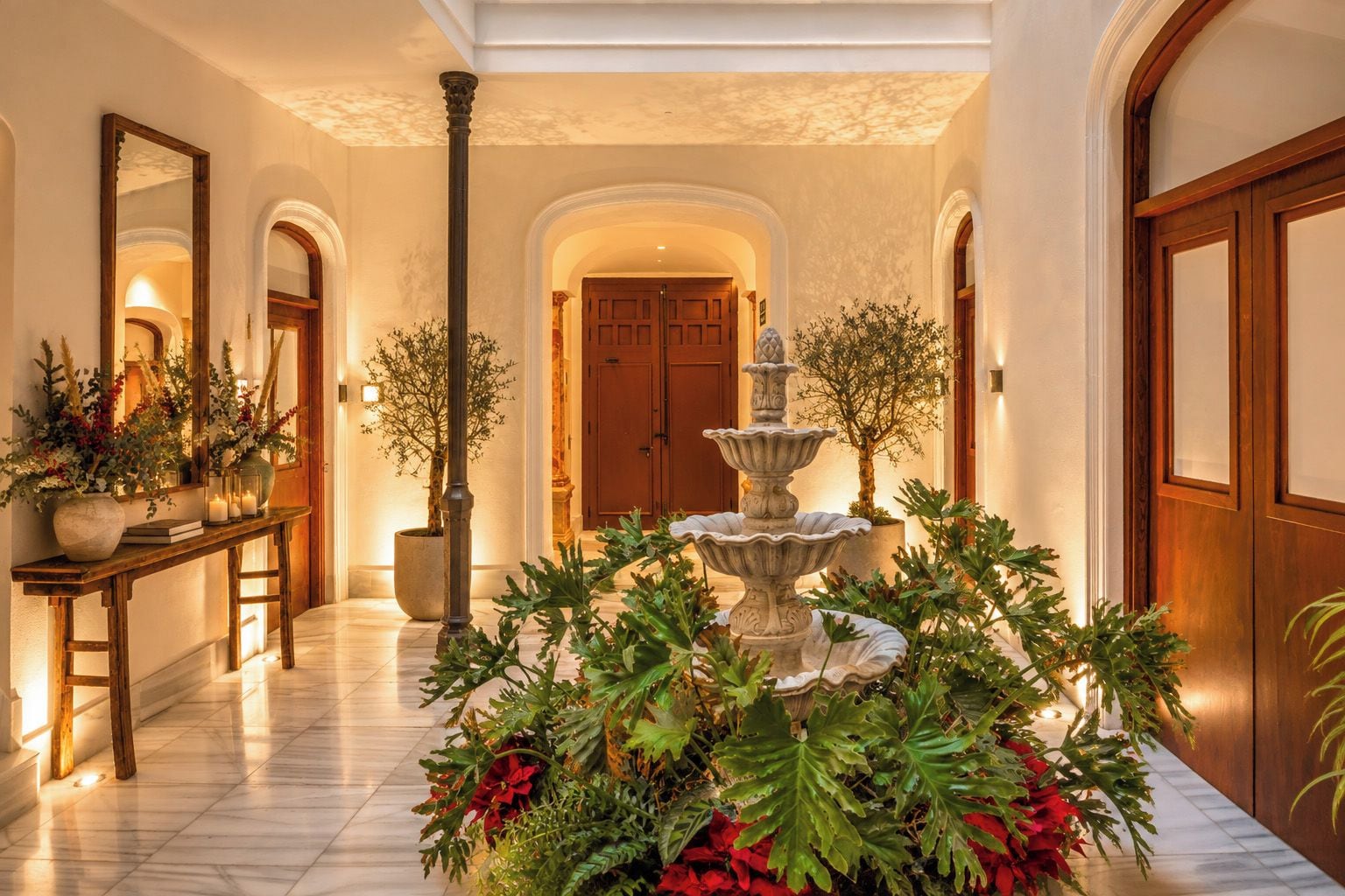 A hallway with a central fountain, a wooden bench, and potted plants.