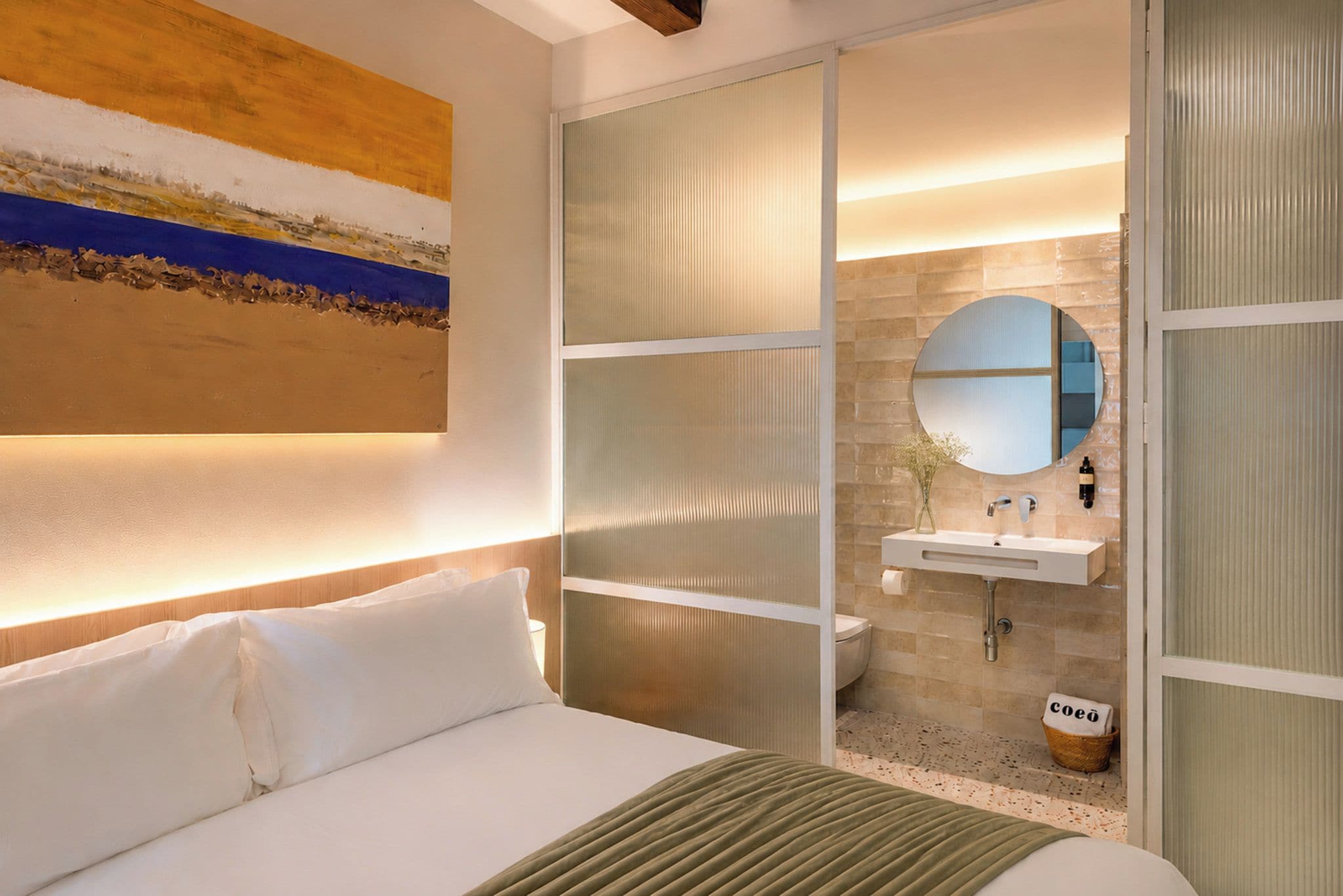Een hotelkamer met een bed, een badkamer met wastafel en spiegel, en een schilderij aan de muur.