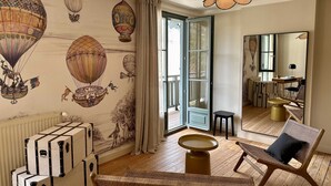 A room with a large window, wicker furniture, and wall art featuring hot air balloons. - LA DEMEURE (Précy-sur-Oise)