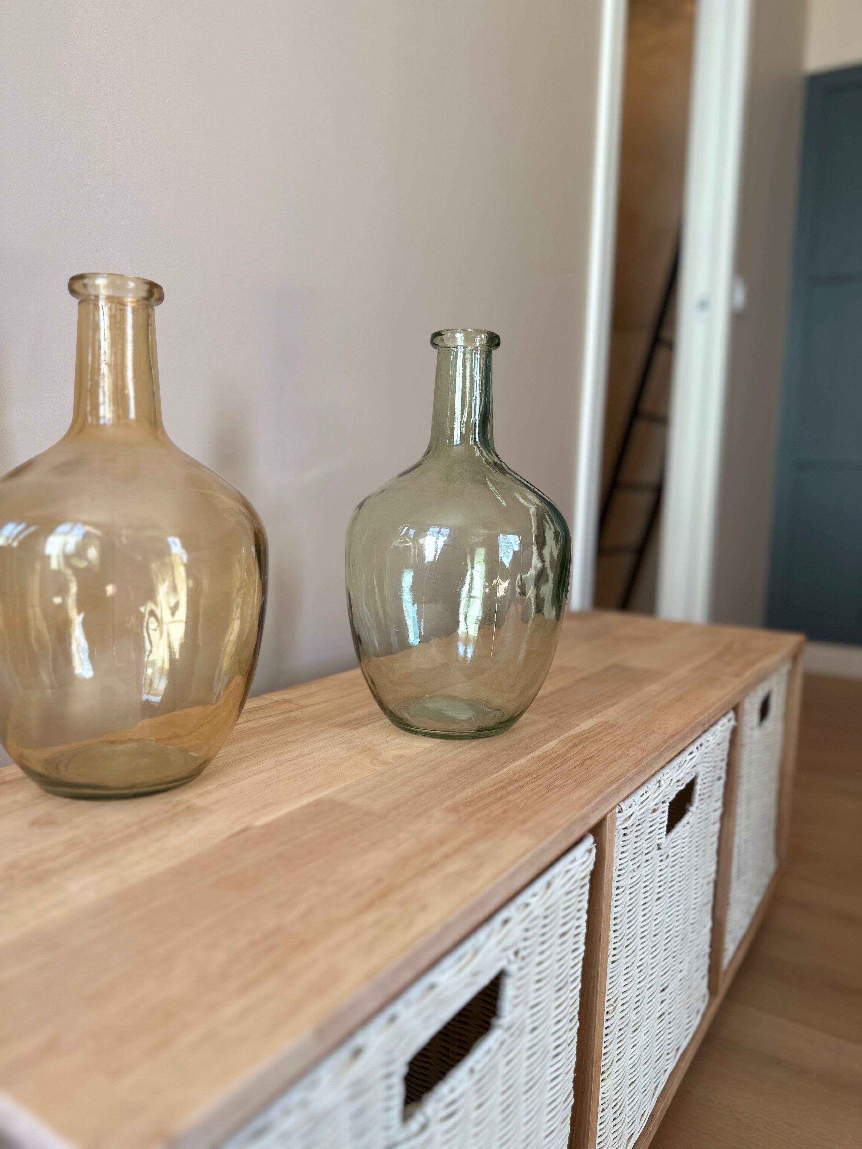 Twee glazen vazen op een houten tafel met witte manden eronder.