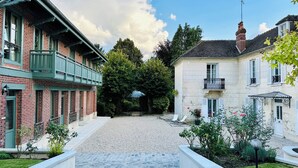 A cobblestone courtyard with a brick building on the left and a stone building on the right. - LA DEMEURE (Précy-sur-Oise)
