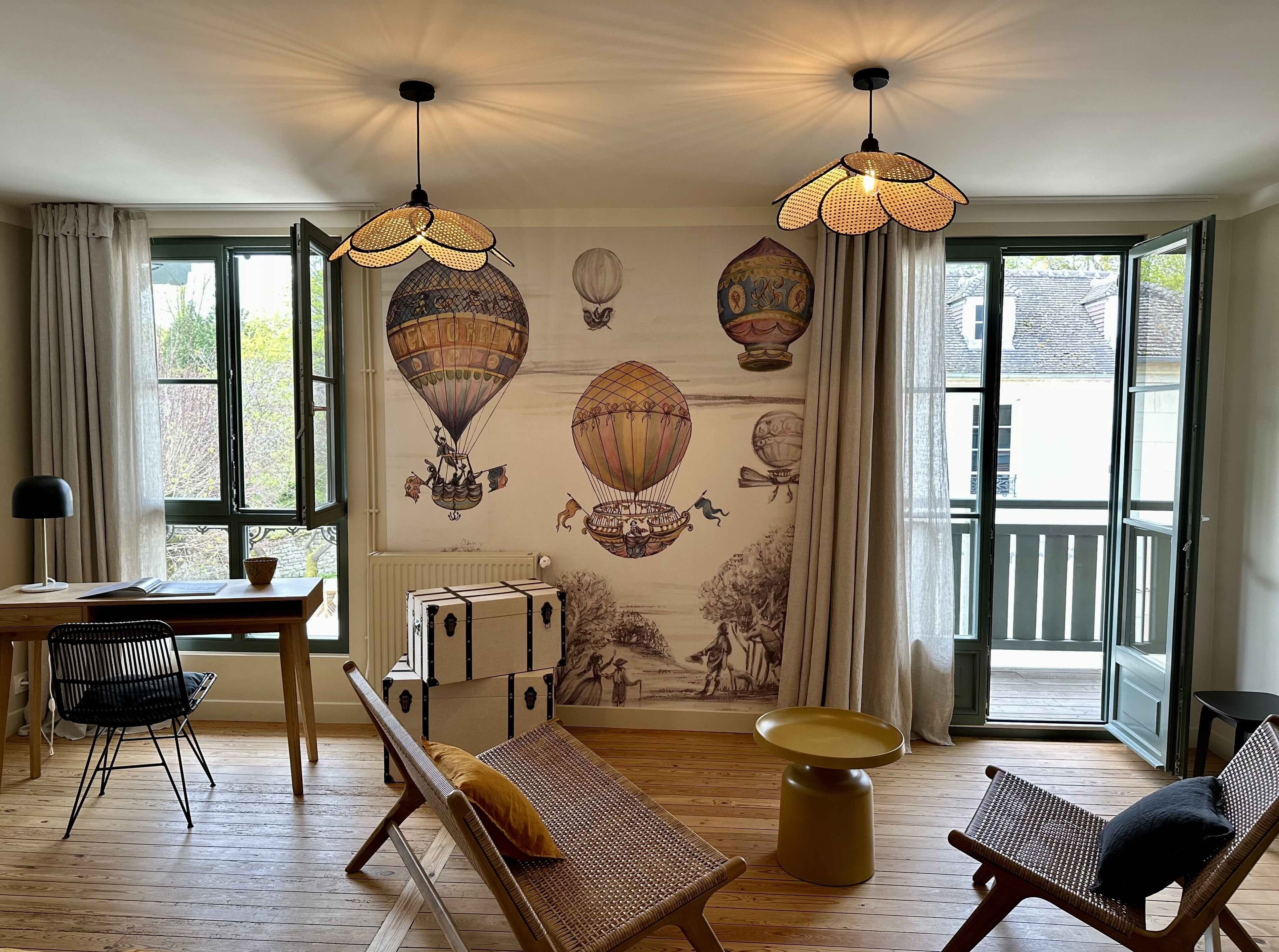 Una habitación con piso de madera, una mesa de comedor con sillas, un sofá, una pequeña mesa redonda y una pared con un mural de globos aerostáticos.