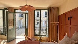 A bedroom with a bed, a hanging light fixture, a window with curtains, and a view of the outside balcony. - LA DEMEURE (Précy-sur-Oise)