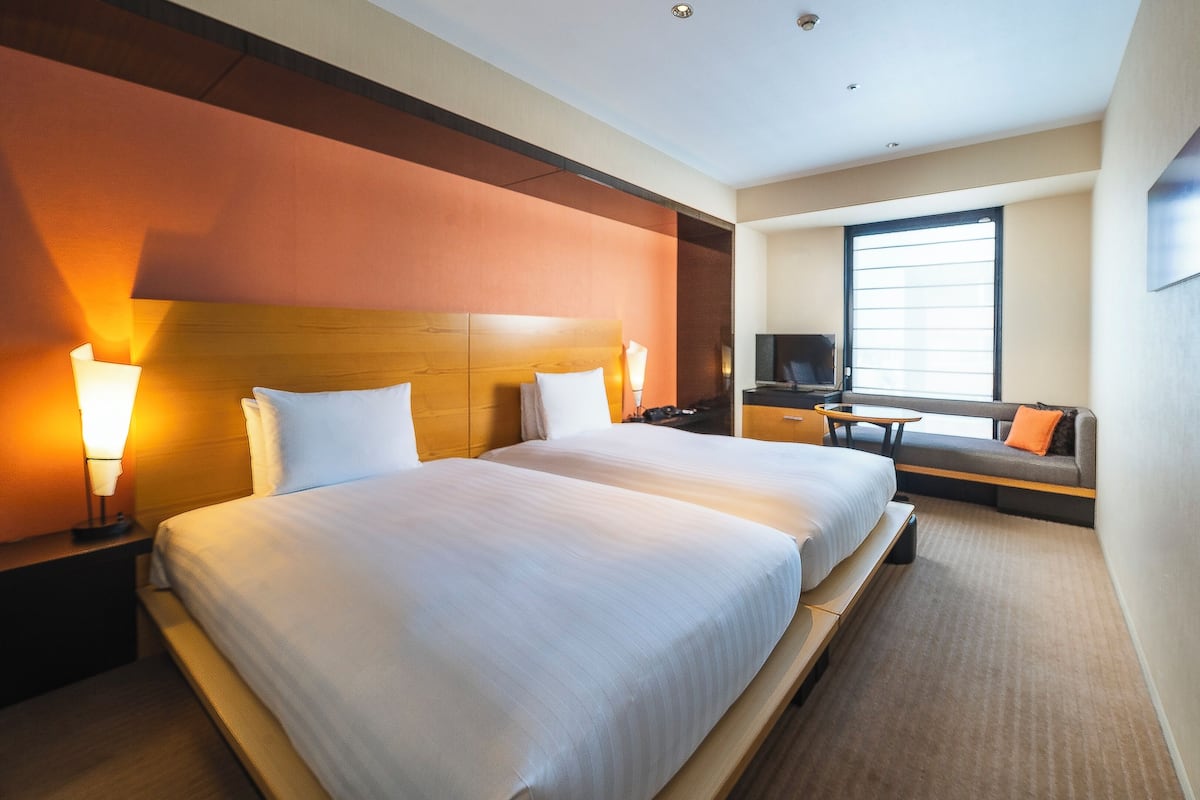 Ein Hotelzimmer mit einem großen Bett, Nachttischlampen, einem Fernseher, einem Sofa und einem Fenster.