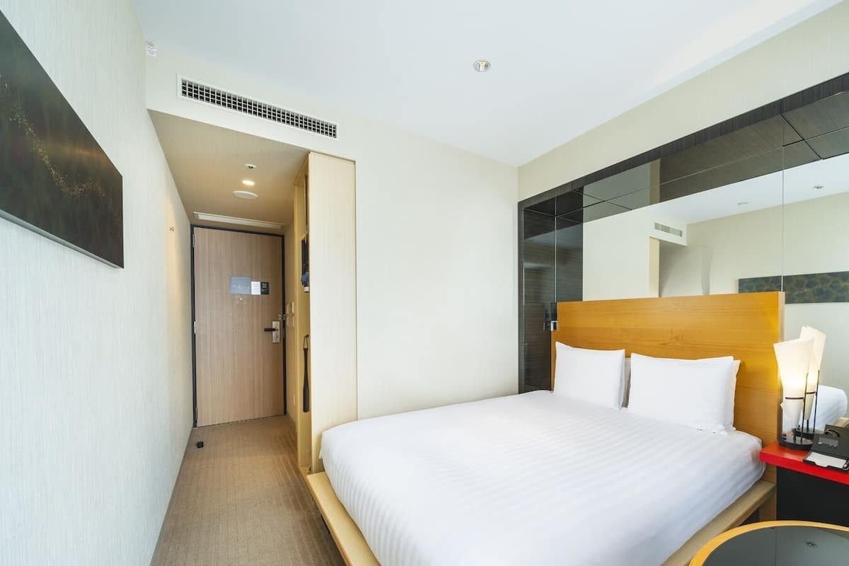 Ein Hotelzimmer mit einem Bett, einem Schreibtisch mit Telefon und einem Spiegel.