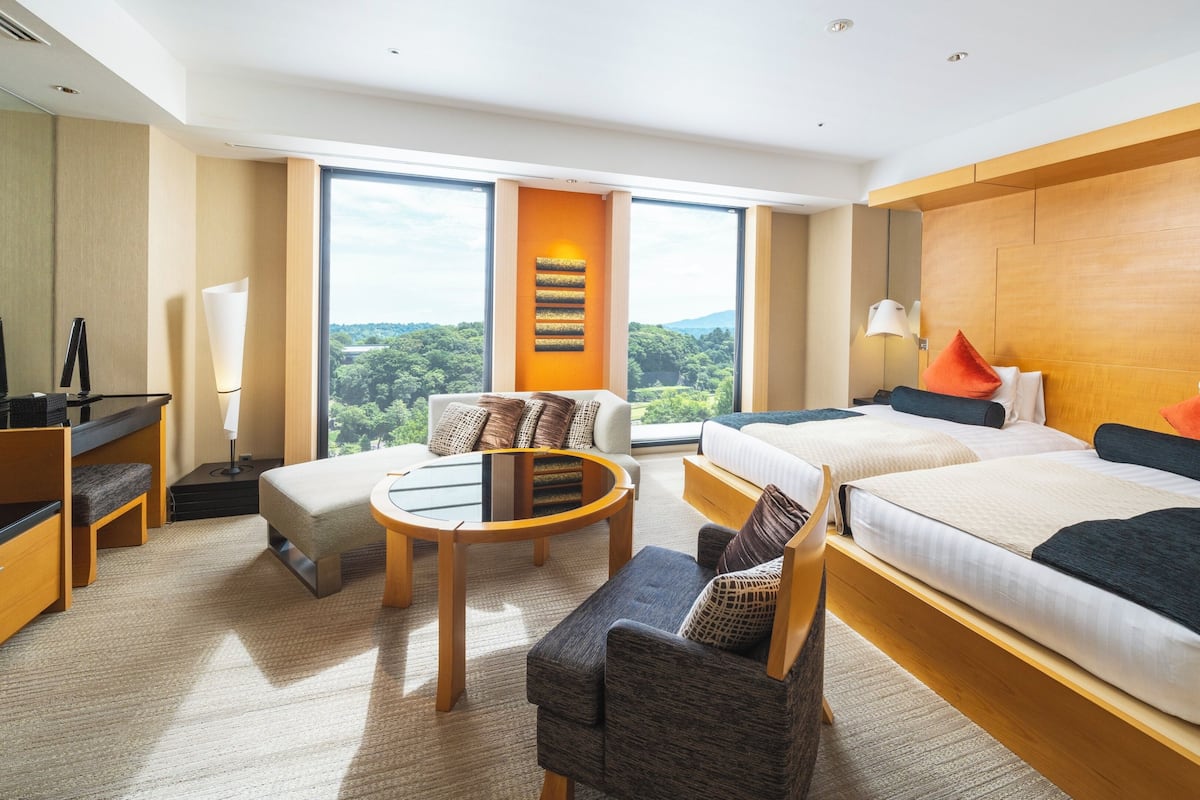 Ein Hotelzimmer mit Bett, Schreibtisch, Stuhl, kleinem Tisch und Blick ins Freie.