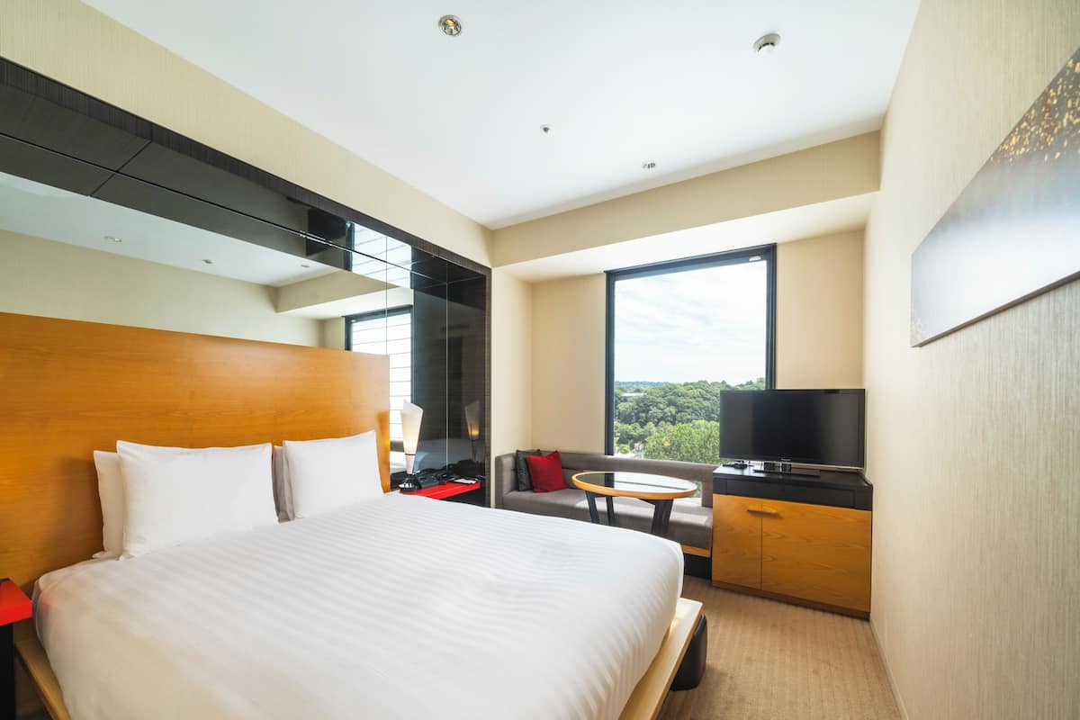 Ein Hotelzimmer mit einem großen Bett, einem Fernseher, einer Sitzecke und einem Fenster mit Blick.